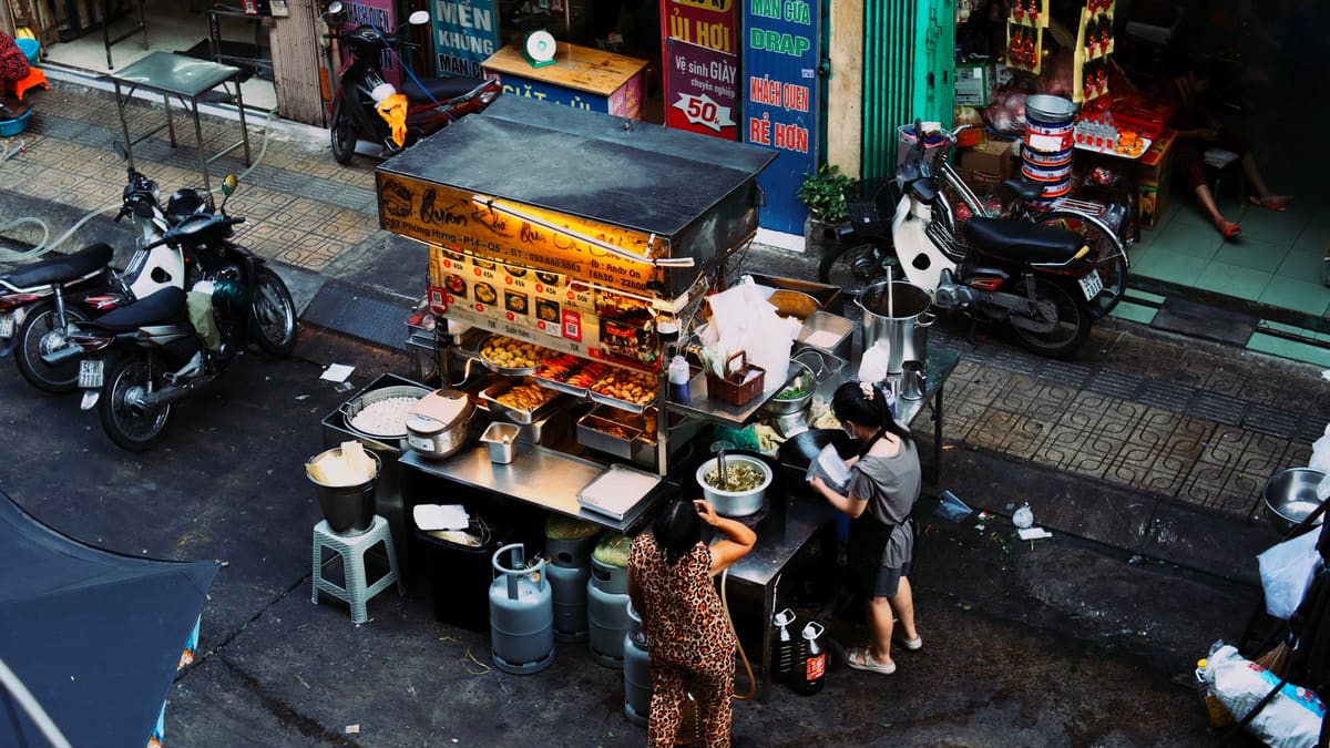 Dua wanita menyediakan makanan di gerai tepi jalan.